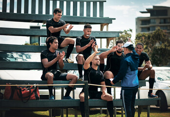 You've done it once again. Cropped shot of a team of rugby players clapping for their coach while sitting on the bench near the field.