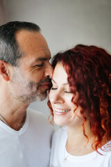 Close-up of a cute European middle-aged couple, tenderness and hugging. Care and emotions. Man and woman together at the window in the bedroom, lifestyle in a real interior.