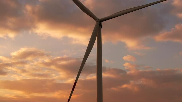 Windmills with huge propellers produce electricity operating at rural station on field at sunset against cloudy sky low angle shot