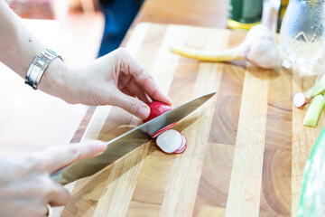 Woman cuts radishes on cutting board on wooden table