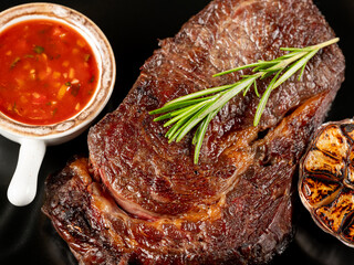 Top view beef steak grill with herbs rosemary, garlic and sauce on black background, overlay, flat lay, close up - 481114716