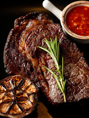 Beef steak grill with herbs rosemary, garlic and sauce on black background. Top view overlay, close up - 481114717