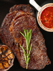 Top view beef steak grill with herbs rosemary, garlic and sauce on black background, overlay, flat lay, close up - 481114718