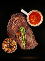 Beef steak grill with herbs rosemary, garlic and sauce on black background. Top view overlay, close up - 481114719