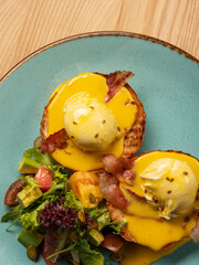 Top view breakfast - eggs Benedict with hollandaise cheese sauce, toast and fresh salad served on plate in restaurant or cafe interior background. Close up, selective focus - 481114777