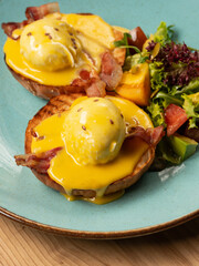 Restaurant breakfast - eggs Benedict with hollandaise cheese sauce, toast and fresh salad. Close up, selective focus - 481114781