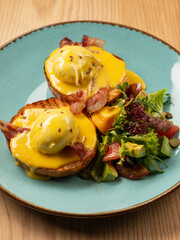 Eggs Benedict with hollandaise cheese sauce, breakfast toast and fresh salad. Close up, selective focus