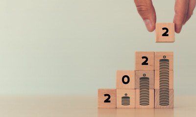 Financial growth concept in 2022. Close up hand arranging wooden cubes stacking '2022' standing on...