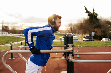 Cheerful young man is training outdoors at the park fitness quipment