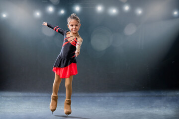 Little skater rides on rings in red and black dress on ice arena