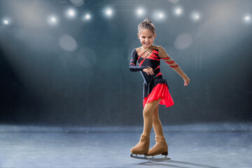 Little skater rides on rings in red and black dress on ice arena - obrazy, fototapety, plakaty