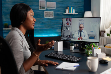 Obraz na płótnie Canvas African american woman talking to medic on video call to receive medical advice about telemedicine and telehealth at home. Young patient using online remote conference to talk to physician