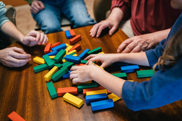 Close up of hands helping build a building of wooden pieces. Famil playing Jenga game. Close-up view of woman and girls hand taking a piece from a Jenga tower.