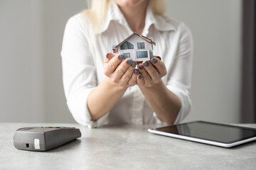 Cropped image of a young woman holding a house model over the comfortable office desk