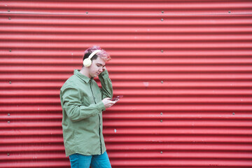 Photo with copy space of a stylish man listening to music with a cellphone next to a red urban wall