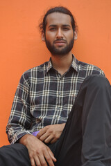 Fototapeta premium Front view of a attractive bearded young man looking at camera, sitting against orange wall background with copy space 