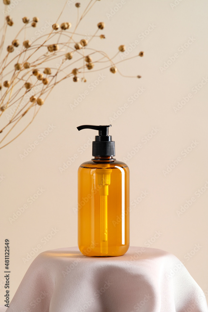 Sticker Cosmetics amber glass bottle on podium and dry grass on beige background. Soap dispenser, shower gel, shampoo container design on dais