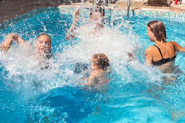 Four happy children having fun in a hotel pool splashing water enjoying summer holidays