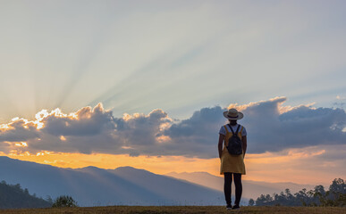 Travel young girl with backpack and hat enjoying sunset on peak mountain. Tourist traveler on...