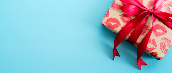 Valentines Day gift wrapped craft paper with lipstick marks print with red ribbon bow on blue background. Valentines day present, surprise. Top view with copy space.