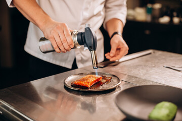Chef fries salmon fish with a gas burner in a modern kitchen. The man prepares food at home. Cooking healthy and tasty food.