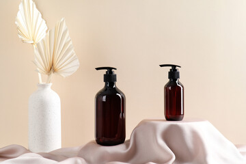 Dark brown cosmetics amber glass bottles on podiums and vase of dried flowers on beige background. SPA bathroom shampoo bottles, shower gel dispenser packaging design