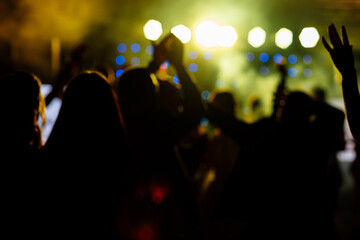 Fototapeta na wymiar cheering crowd in front of bright yellow stage lights. Silhouette image of people dance in disco night club or concert at a music festival.
