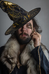A young dark-haired man in a witch's hat looking through a dried bird's foot.  Selective focus