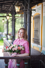 Young happy blonde woman in a pink dress with a large bouquet of flowers walks around the old European city and enjoys life on a summer day, beautiful portraits with a huge bouquet of flowers.