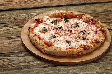 Uncut Italian pizza served with fresh basil leaf on Wooden board on dark texture background. Hot pizza with tomatoes and pesto sauce