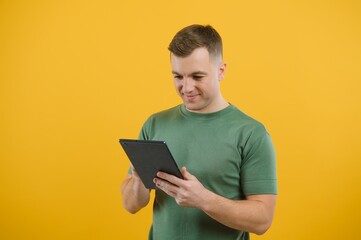 Amazed happy man using digital tablet looking shocked about social media news, astonished man shopper consumer surprised excited by online win isolated over yellow background.