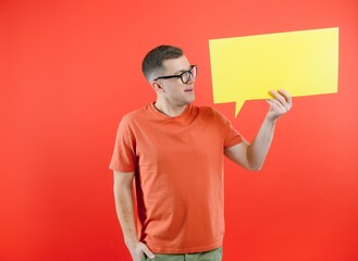 Happy smiling man holding yellow bubble speech, looking at camera over red background