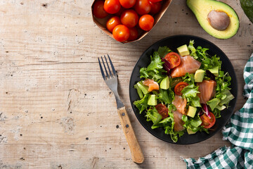 Salmon and avocado salad in plate on wooden table. Top view. Copy space