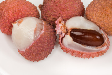 Two partly peeled ripe lychee fruits against the whole fruits