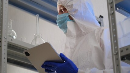Scientist or medical worker, in protective uniform, makes notes in a tablet in a science laboratory. Close-up of a male scientist or doctor recording the results in an electronic journal
