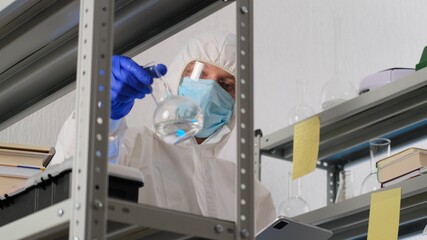 Man scientist or medical working, in protective uniform, looking into the frame in science lab. Close up of male scientist or doctor doing laboratory research and writes results in the journal.