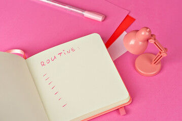 Notebook on a pink background. Toy table lamp near the notebook. Copy space and free space for text in notebook. Mockup for design. The word "routine" is written in pencil. Creativity concept.