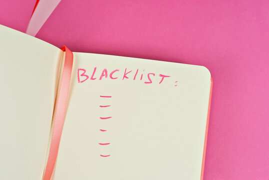 Notebook on a pink background. Toy table lamp near the notebook. Copy space and free space for text in notebook. Mockup for design. The word "black list" is written in pencil. Creativity concept.