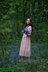 A young girl walks in a field of blue flowers at dusk.