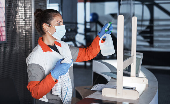 She routinely keeps the space clean. Shot of a young woman cleaning the reception desk in a gym. - Powered by Adobe