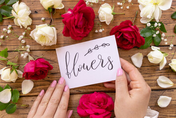 Hands with card FLOWERS near red and cream flowers close up on a wooden table