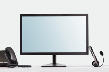 Computer monitor mockup for your design and VOIP headset phone on desk at modern office. Contemporary workplace or call centre operator with PC and headphones. Telecommunications support