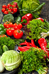 Cabbage, peppers, tomatoes, cucumbers, lettuce, cherry tomatoes, broccoli, arugula on a black background. variety of vegetables on a pile on a wooden table.