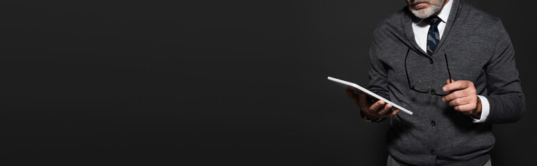 cropped view of bearded senior man with eyeglasses and digital tablet isolated on black, banner.