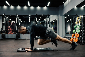 A sporty man does fitness exercises on a mat in a gym.
