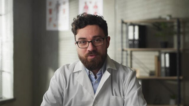 Young male doctor speaking looking at camera in web chat consulting client online. Telemedicine concept