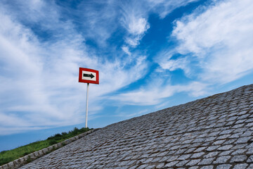 Black arrow on white background and in red frame standing atop of cobblestone paved hill at day. Blue sky with great clouds. Copy space, concept
