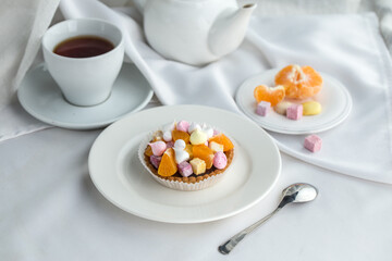 Mini fruits tart dessert with orange slice and meringue and cup of tea on the table