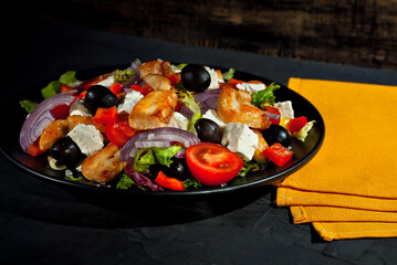 Salad with tomatoes, peppers, olives and chicken fillet. Fresh salad in a black plate on a dark background. Yellow towel near the plate.