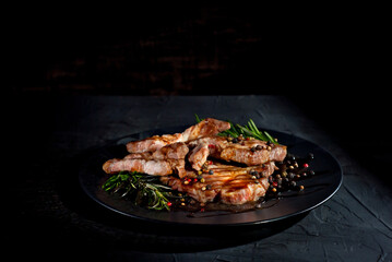 Steak with sauce on a black plate. Meat with spices and rosemary on a dark background. Contrasting light as an artistic effect. Copy space and free space for text near food.